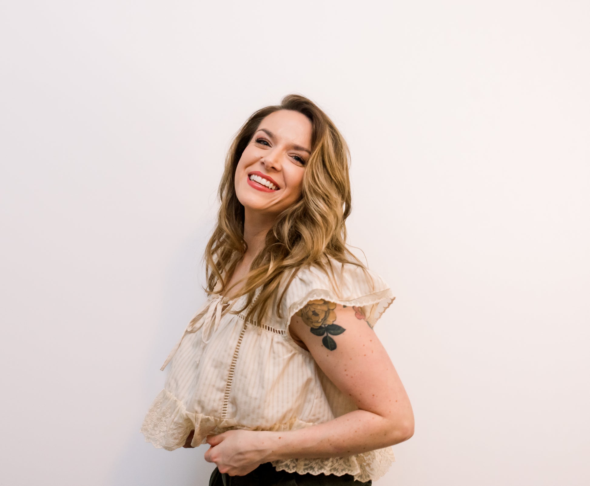 Woman with a tattoo on her arm wearing a beige blouse against a white background